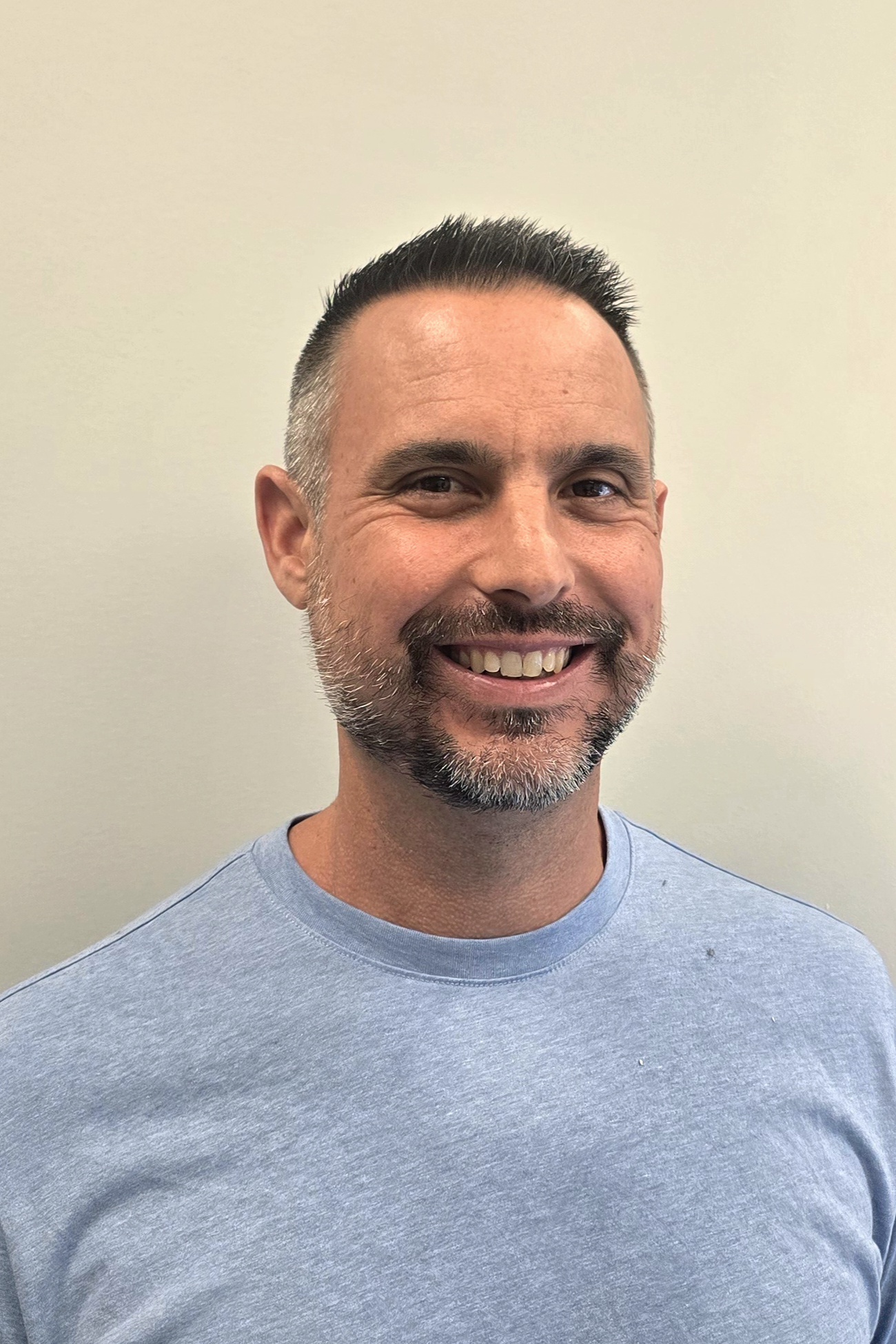 Smiling man in a light blue shirt against a neutral background, possibly a home builder.