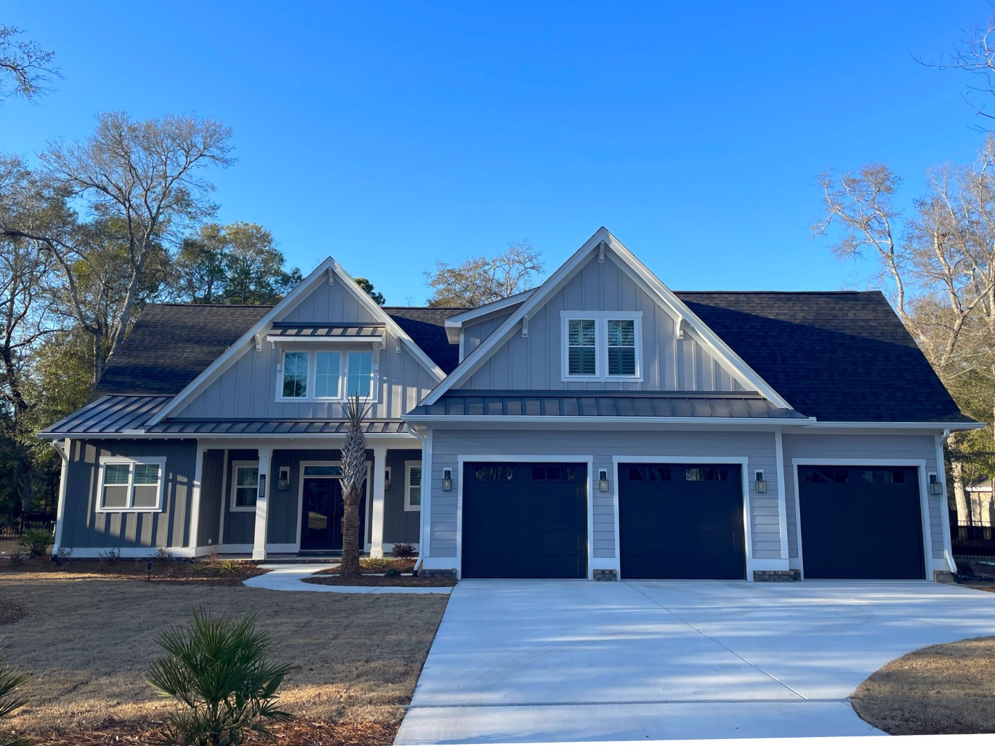 Modern gray house with three-car garage, gabled roof, and white trim, set in a wooded area. Ideal for a home builder project.