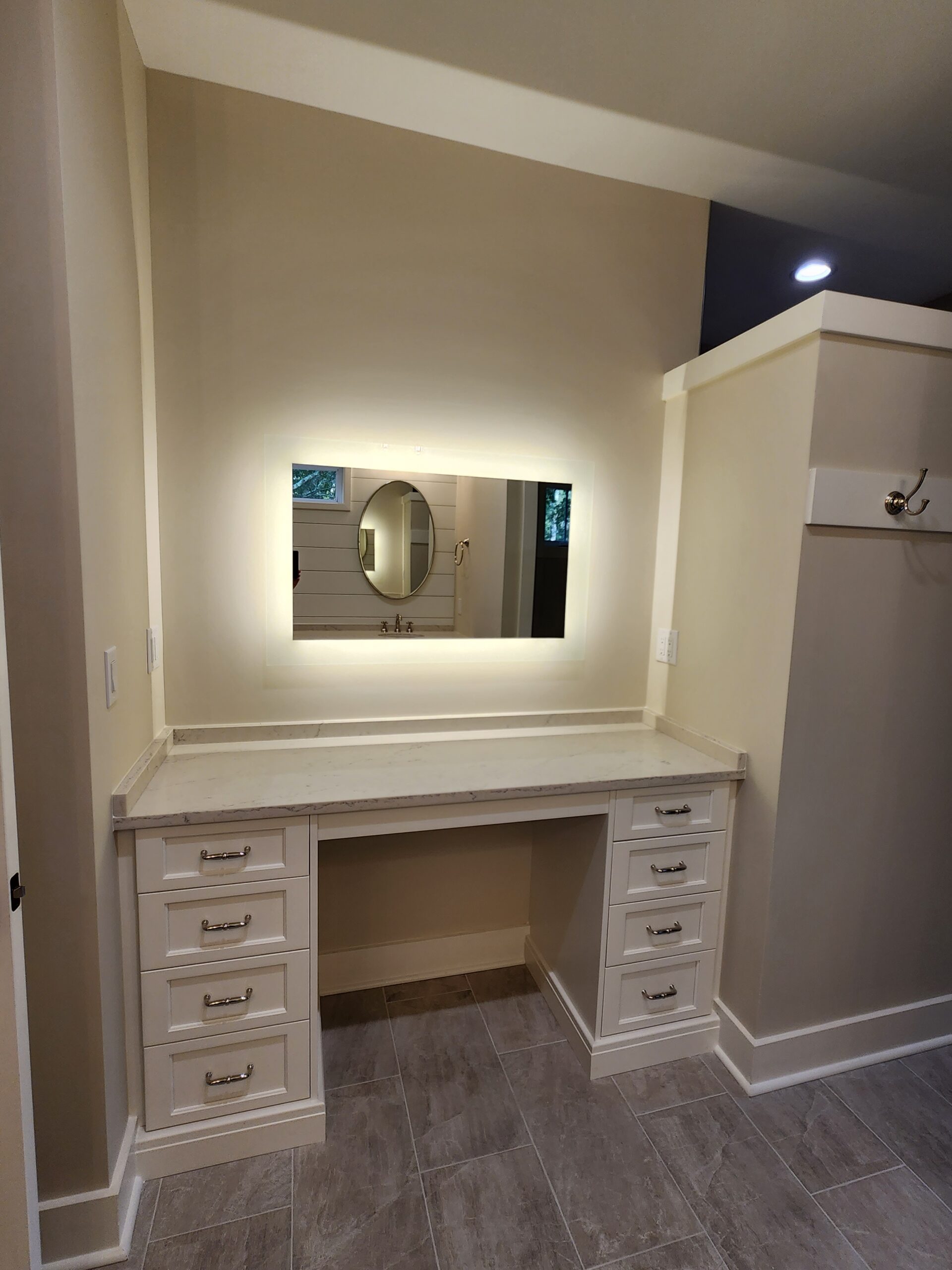 OceanHarbourEstates (5) Vanity setup with cream drawers and marble top, illuminated mirror reflecting round window, showcasing a home builder's craftsmanship.