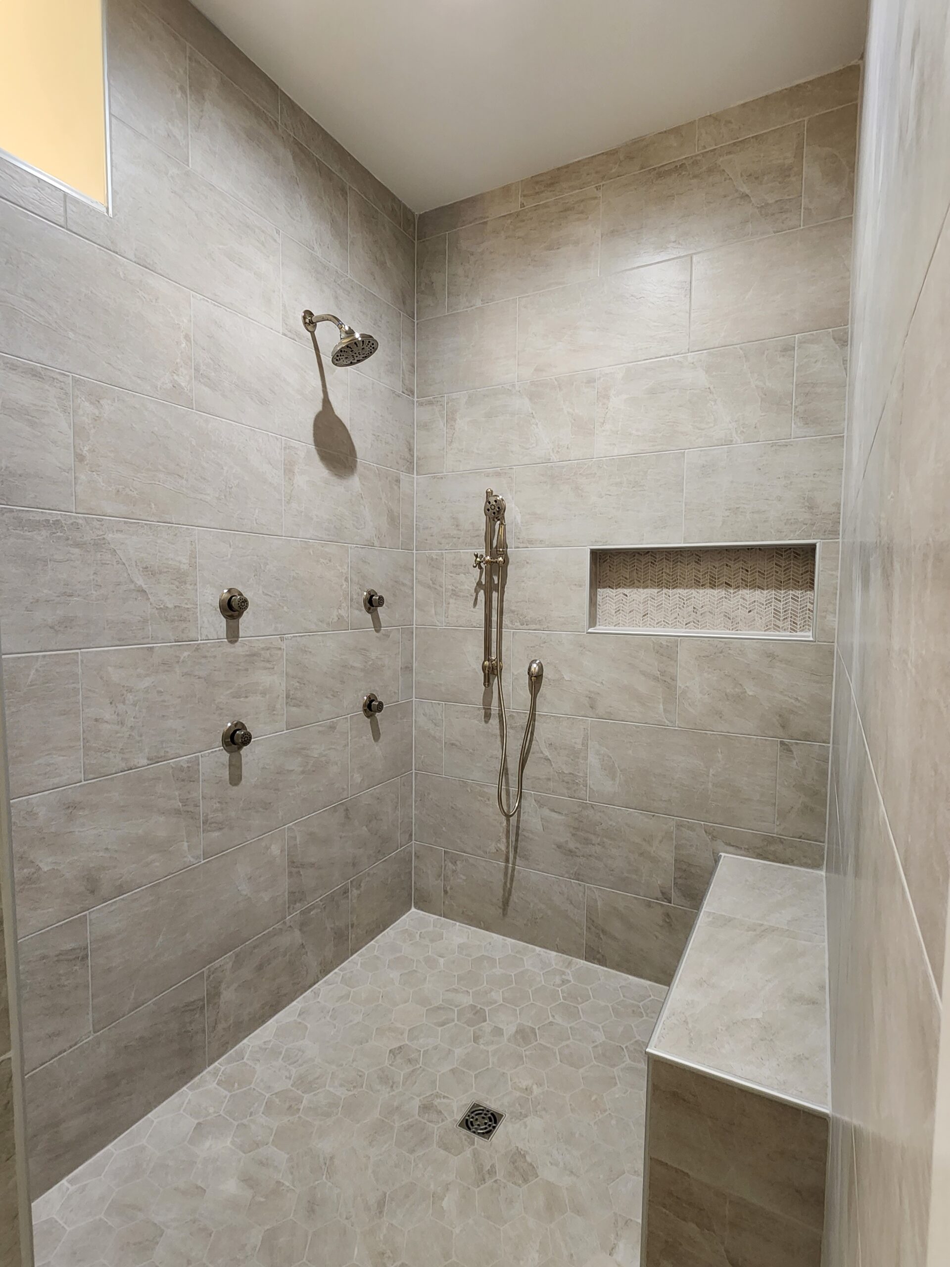 OceanHarbourEstates (6) Spacious tiled shower with built-in bench, niche, and multiple showerheads, showcasing a home builder's modern bathroom design.