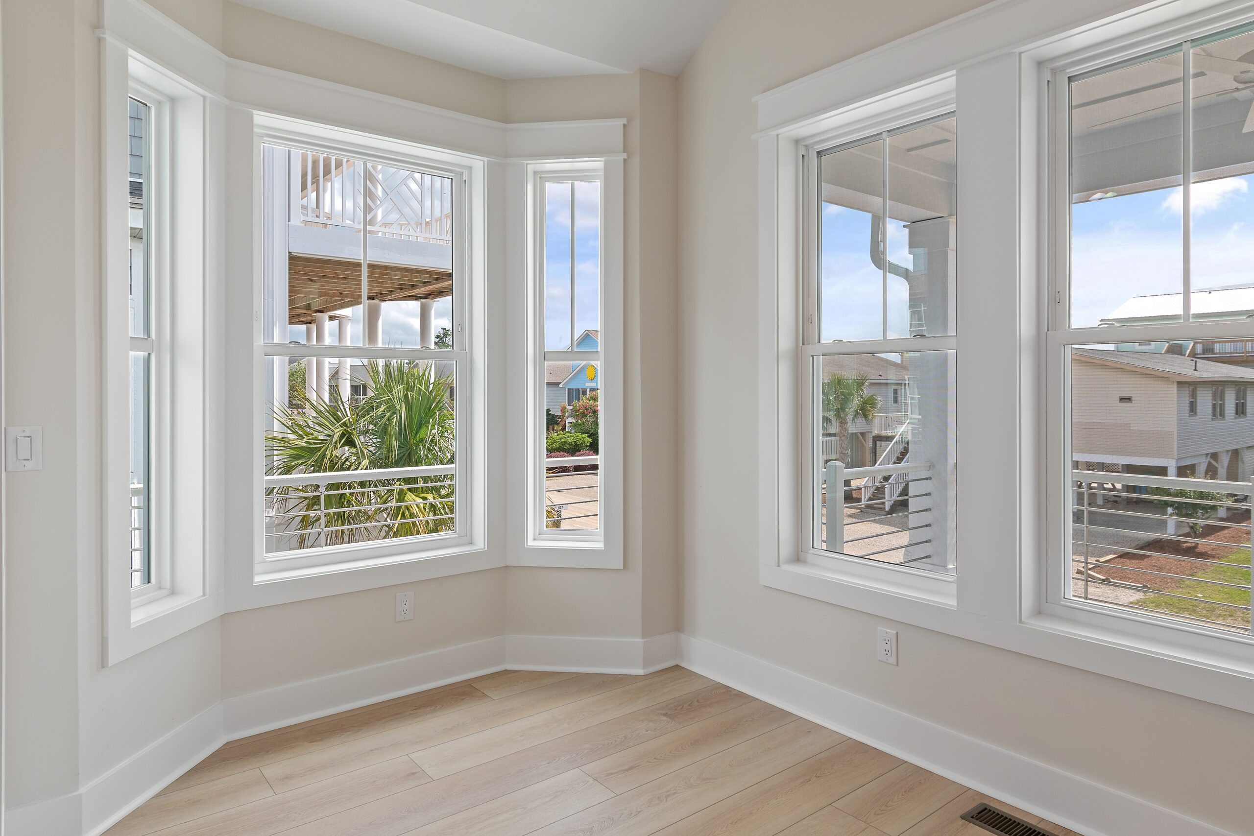 Sunlit room with large windows, light wood floors, and views of a developing neighborhood, showcasing home builder architecture.